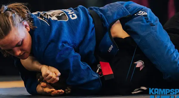 Två kvinnor i blå och svarta gi tävlar i bjj sm. En kämpar sig framåt, fokuserad på att vinna.