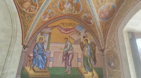 Mozaika przedstawia scenę biblijną z postaciami w stylu sztuki sakralnej. Widać Matkę Boską, anioła i mężczyznę, a także symbole religijne.