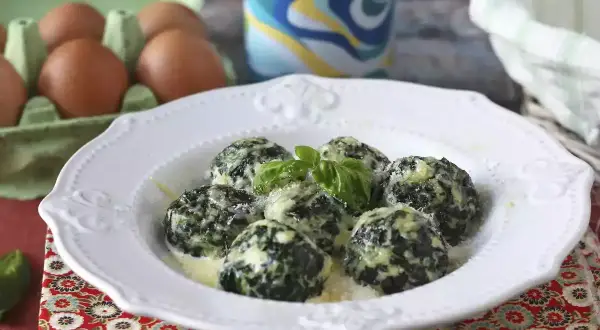 Spenat recept: Krämiga spenatbollar med basilika och parmesan på en vit tallrik. Ägg i bakgrunden.