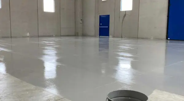 Pavimento in resina epossidica appena posato, lucido e riflettente. Un secchio di prodotto è visibile in primo piano, pronto per risolvere eventuali problemi di applicazione.