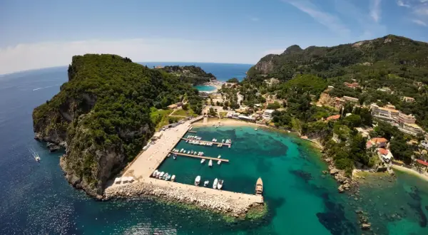 Malownicza zatoka na Korfu, idealna na wakacje z dzieckiem. Widać tu port z łodziami, plażę i zielone wzgórza.