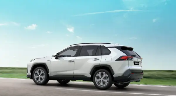 Biały Suzuki Across jedzie po drodze, a jego sylwetka lśni niczym ignis na tle błękitnego nieba.