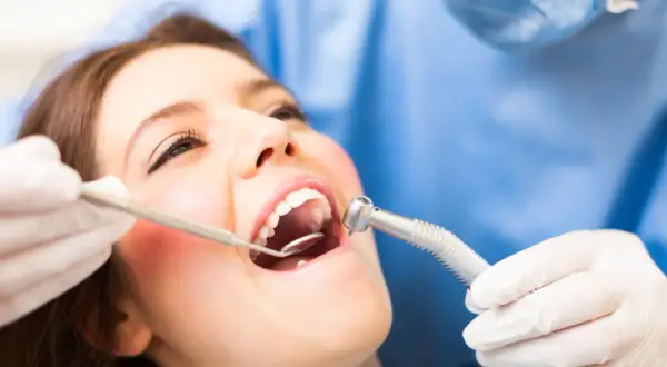 Pacjentka u dentysty, który bada jej dziąsło. Może to być związane z ropniem na dziąśle domowe sposoby.
