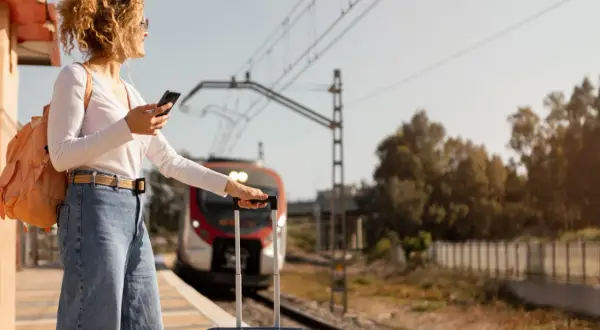 Kobieta z plecakiem i walizką czeka na pociąg PKP. Jej bagaż ponadwymiarowy jest gotowy do podróży.