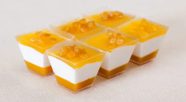 Sechs kleine Dessertgläser mit weißer Creme und Mango-Topping, garniert mit kleinen Fruchtstückchen.