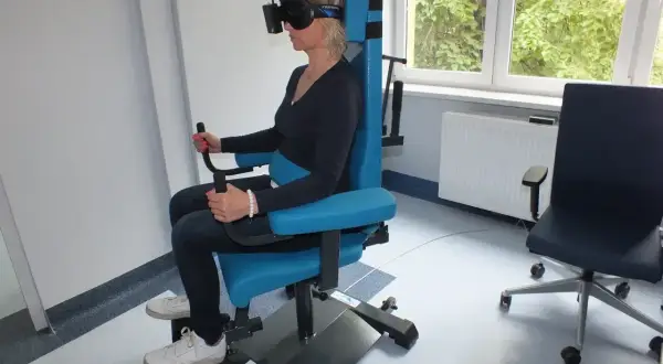 Kobieta w goglach VR na specjalnym fotelu wykonuje badanie vng. Gdzie zrobić takie badanie?