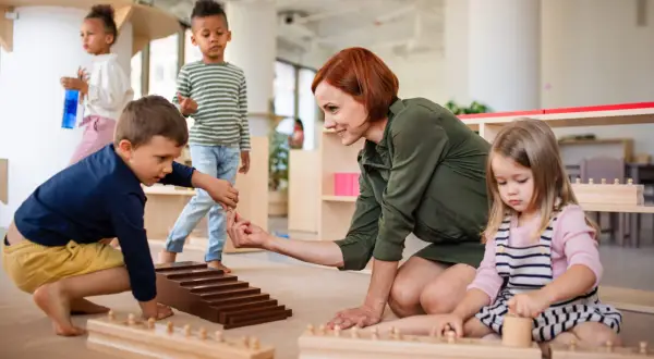 Niños y maestra en el suelo, aprendiendo con materiales didácticos. Las rutinas diarias en el aula fomentan el desarrollo.