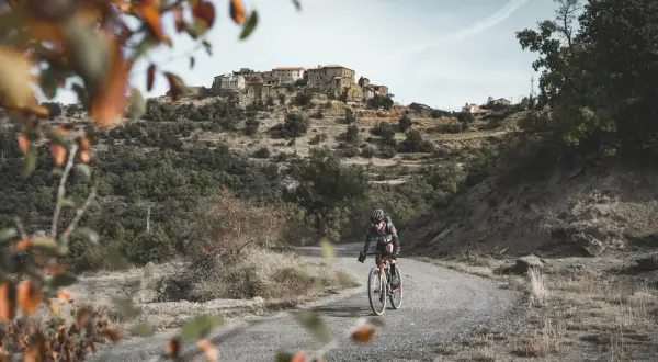 Ciclista en ruta de gravel, disfrutando del paisaje montañoso y el pueblo al fondo. Una aventura de montsec bikepacking loop.