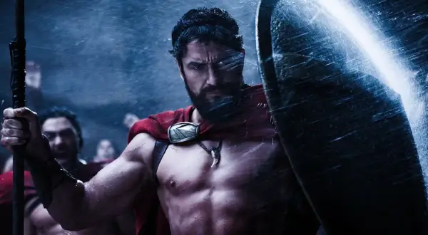 Gerard Butler jako Leonidas w filmach "300". Spartanin w deszczu, z tarczą i włócznią, gotowy do walki.