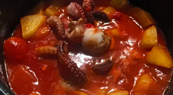 Un saporito stufato di polpo e patate in un sugo rosso brillante. I tentacoli del polpo sono ben visibili, immersi tra i pezzi dorati di patate.