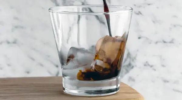 Mörk, rik cold brew kaffe hälls över is i ett glas.