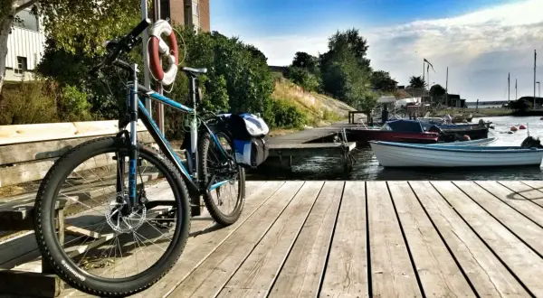 Rower z sakwami czeka na przygodę w Karlskronie. Drewniany pomost, łodzie i błękitne niebo zapraszają do odkrywania uroków wybrzeża.