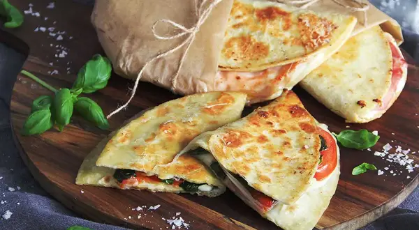 Läckra piadina recept på en träskärbräda, inslagna i papper med snöre. Basilika och flingsalt dekorerar.