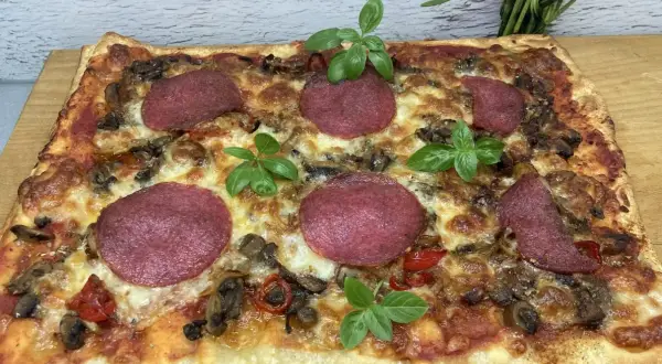 Prostokątna pizza z salami, pieczarkami i papryką, ozdobiona listkami bazylii. Idealne dodatki dla miłośników klasyki.