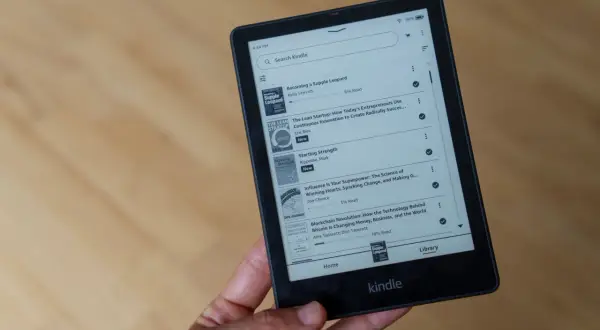 Main d'une personne tenant un livre format Kindle affichant une liste de titres, dont "Becoming a Supple Leopard" et "The Lean Startup".