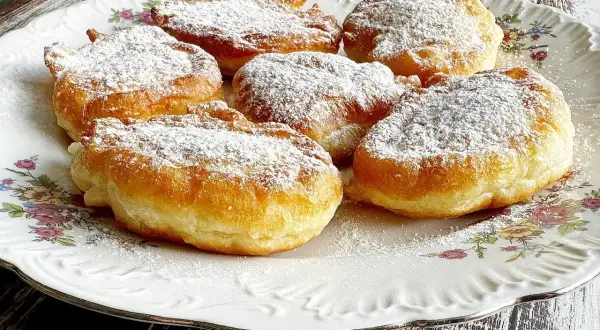 Puszyste racuchy na jogurcie, posypane cukrem pudrem, kuszą swoim złotym kolorem i delikatnością. Idealne na deser!