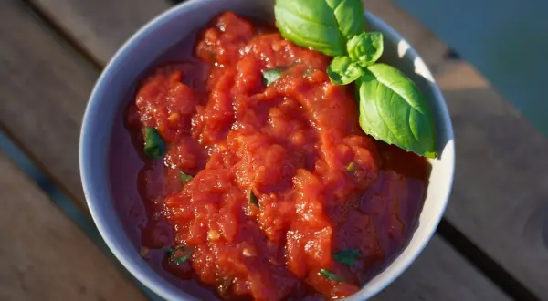 Schüssel mit frischer, stückiger Tomatensoße, wie in der Pizzeria, garniert mit Basilikum. Perfekt für hausgemachte Pizza.