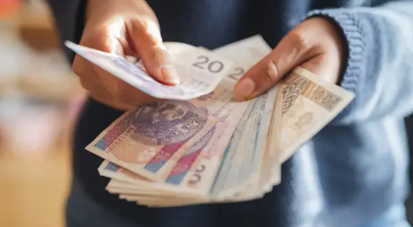 Dłonie trzymające stos polskich banknotów.