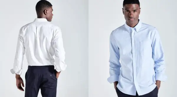 Ein Mann präsentiert ein weißes und ein hellblaues Button-Down-Hemd. Dieses Hemd mit Knopfleiste ist ein Klassiker.
