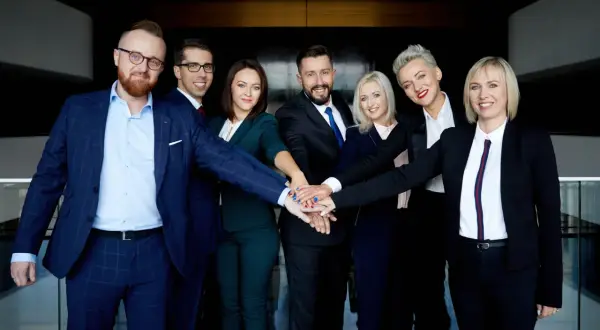 Grupa prawników w garniturach i kostiumach z rękami złożonymi na środku.