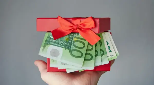 Czerwone pudełko z prezentem i banknotami euro na dłoni.