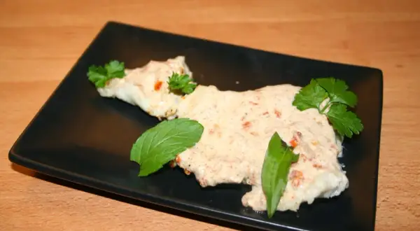 Zarter Fisch mit cremiger Joghurtsoße, garniert mit frischen Kräutern auf schwarzer Platte.