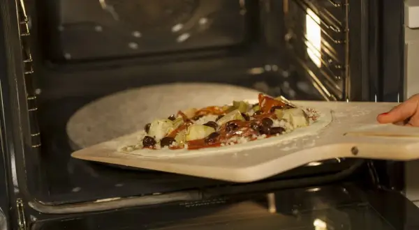 Pizza z dodatkami na łopacie do pizzy, gotowa do wsunięcia na kamień do pizzy granitowy w rozgrzanym piekarniku.