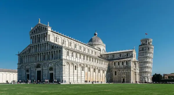 La piazza dei Miracoli a Pisa con il Duomo e la celebre torre di Pisa, simbolo della città, sotto un cielo azzurro.