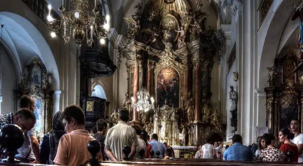 Ludzie uczestniczą w liturgii mszy świętej w bogato zdobionej, barokowej świątyni.