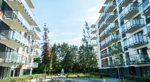 Nowoczesne apartamentowce z balkonami i szklanymi balustradami, otoczone zielenią. Idealne miejsce na inwestowanie w nieruchomości.