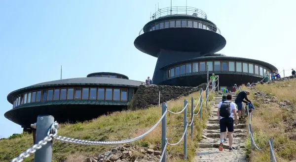 Wanderer steigen die Steintreppe zur Schneekoppe Seilbahn hinauf. Die futuristischen Gebäude auf dem Gipfel sind schon zu sehen.