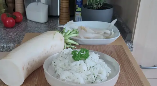Ein frischer Rettich liegt neben einer Schüssel mit cremigem Rettichsalat, garniert mit Petersilie. Perfekt für ein leichtes Rettichsalat Rezept.