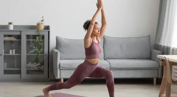 Femme pratiquant le yoga à la maison gratuit, en posture de guerrier, dans un salon moderne.