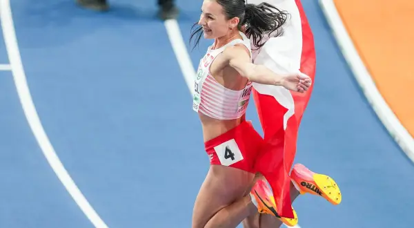 Polska biegaczka w skoku radości, z biało-czerwoną flagą. Numer 4 na spodenkach.