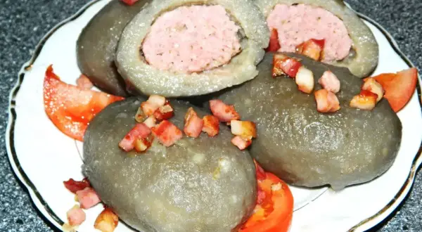 Cepelin z mięsem, polany skwarkami i podany z pomidorem. Pyszne danie kuchni litewskiej.