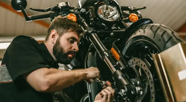 Mechanik z brodą pracuje przy motocyklu. Rozrusznik kręci, a motocykl nie odpala.