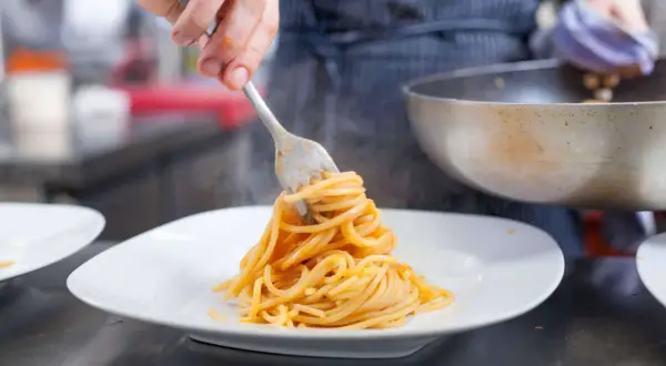 Eine Gabel hebt dampfende Spaghetti, ein Klassiker der Pasta italiana, auf einen weißen Teller.