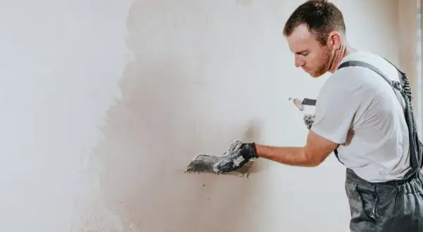 Operaio con spatola applica intonaco su muro. La rasatura è un passaggio cruciale per una finitura perfetta.