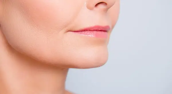 Primer plano de labios rosados y piel con un ligero surco nasogeniano, mostrando detalles de la textura facial.