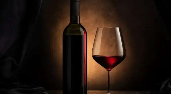 Una bottiglia e un calice di vino rosso, immersi in un'atmosfera suggestiva che esalta i profondi colori vino rosso.
