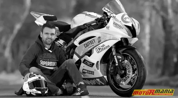 Czarno-białe zdjęcie motocyklisty Williama Dunlopa siedzącego obok swojego motocykla wyścigowego.