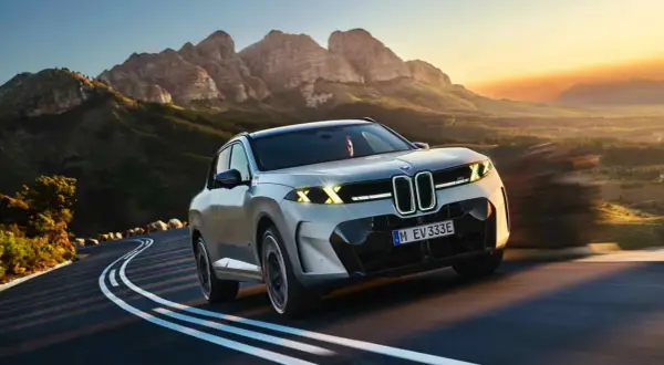Nowe BMW X5 na krętej drodze wśród gór o zachodzie słońca.