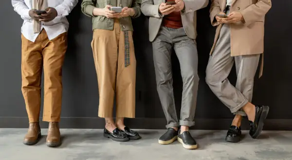 Cztery osoby w eleganckich strojach, trzymające telefony. Wszyscy przestrzegają dress code elegant.