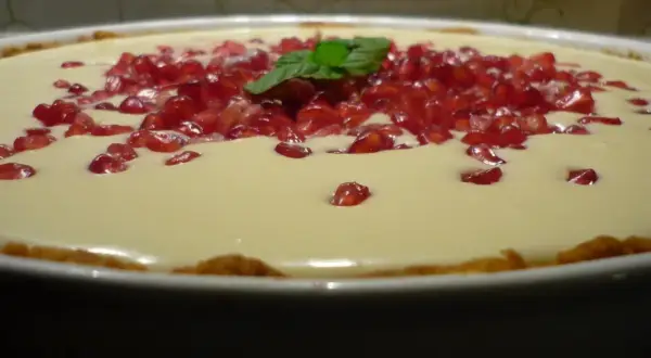 Pyszna tarta z kremem z białej czekolady, ozdobiona pestkami granatu i listkiem mięty.