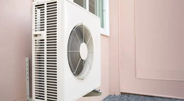 Unité extérieure d'une pompe à chaleur, installée sur un mur rose. Le ventilateur est visible, prêt à assurer le confort thermique.