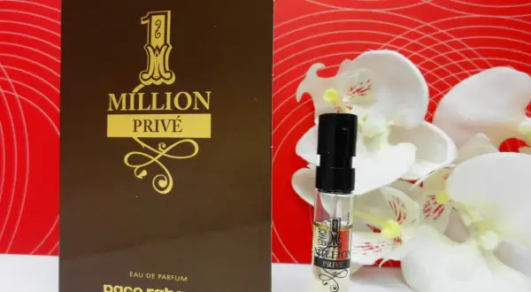 Złoty flakonik i próbka Paco Rabanne 1 Million Privé na tle czerwonych fal i białych kwiatów.