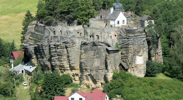 Felsenburg Einsiedlerstein thront auf einem Sandsteinfelsen, umgeben von grünen Hügeln und Wäldern.