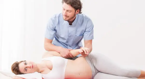Fisioterapeuta ayuda a una mujer embarazada con un masaje perineal, preparándola para el parto.