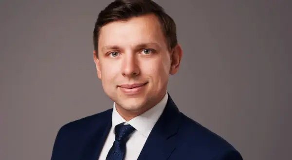 Portret mężczyzny w granatowym garniturze i białej koszuli z krawatem.