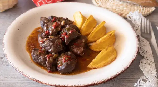 Sabrosa carne de cabra estofada en salsa con trozos de pimiento rojo y verde, acompañada de patatas gajo doradas.